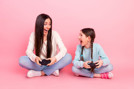 Charming mother and daughter enjoying quality time while playing video games on pink background
