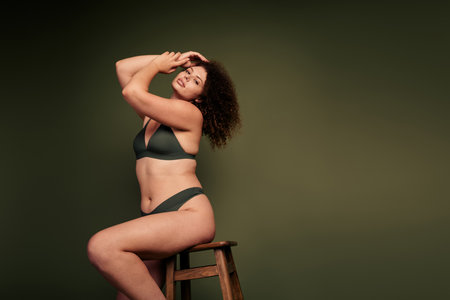 Confident and Beautiful Plus Size Woman in Lingerie Seated in Front of a Khaki Background, Embracing Self Love and Natural Beautyの写真素材