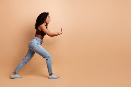 Young stylish woman with curly hair posing in a beige studio while wearing casual jeans and a crop topの写真素材