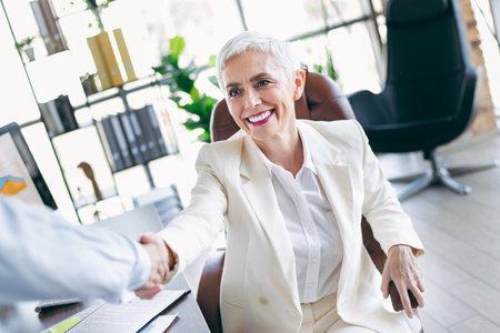 Successful mature businesswoman shaking hands in elegant formalwear, showcasing professionalism and successの写真素材