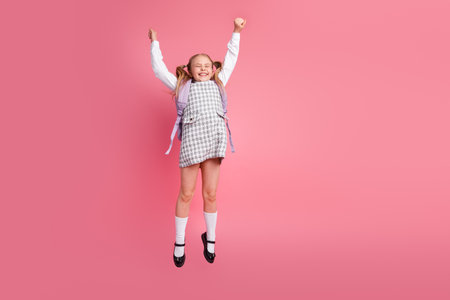 Cheerful young schoolgirl in uniform jumping joyfully with excitement on a pink backgroundの写真素材