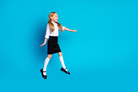 Excited young schoolgirl in uniform jumping with joy against a blue background reflecting happiness...