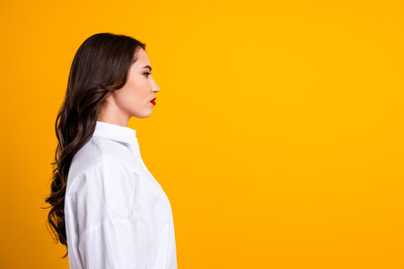 Stylish young woman in a white shirt on an orange backdrop showcasing elegance and charmの写真素材