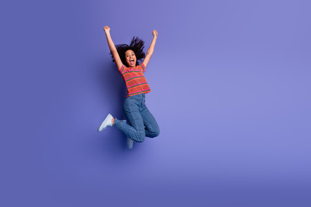 Energetic young woman jumping joyfully against a vibrant violet background, expressing happiness
