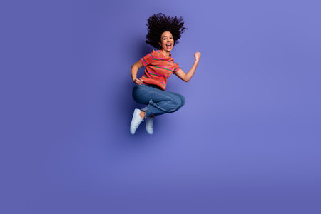 Young woman jumping joyfully in casual outfit with vibrant purple background showing happiness and energyの写真素材