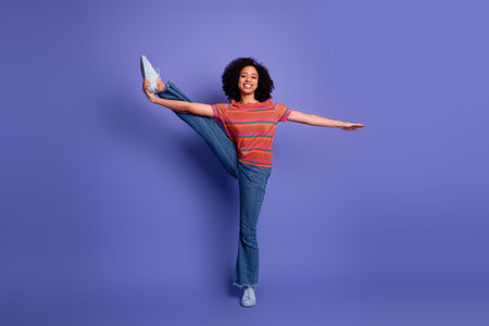 Young woman in casual outfit posing with a vibrant stretch, smiling joyfully against a solid purple...