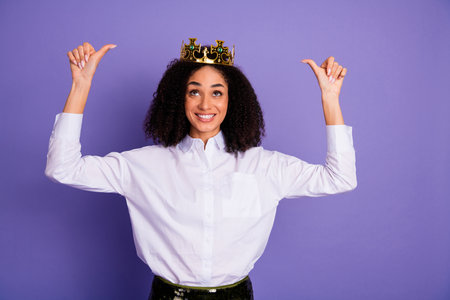 Confident businesswoman wearing a crown and pointing at herself on a vibrant purple backgroundの写真素材
