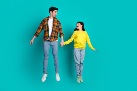 Young couple holding hands and jumping with joy against a bright turquoise background, expressing fun and joyful bondingの写真素材