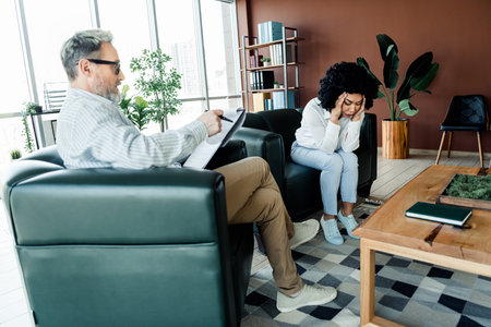 Professional Therapist Consults a Concerned Client During a Counseling Session in a Modern Office with Comfortable Decorの写真素材
