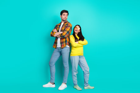 Happy couple standing confidently against turquoise background showcasing casual style and playful...