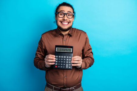 Young businessman holding a calculator with a playful grin on a teal background conveying humor and professionalismの写真素材