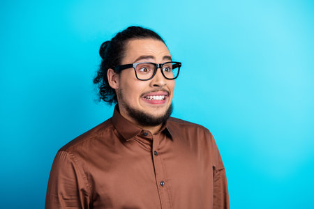 Professional young man with a humorous expression in elegant attire standing against a vibrant turquoise backgroundの写真素材