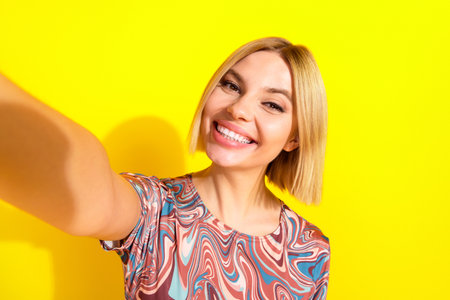 Vibrant portrait of a carefree young woman taking a cheerful selfie against a bright yellow vibrant...