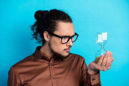 Young professional holding an hourglass while wearing stylish eyewear on a turquoise background