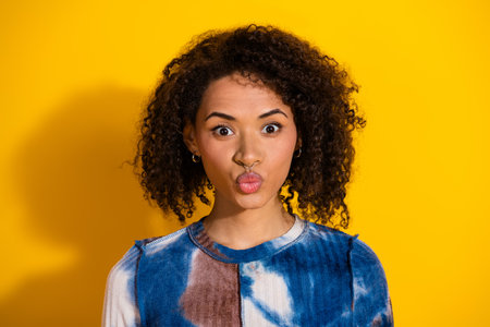 Young woman with expressive pose and curly hair stands against a vibrant yellow background wearing a...