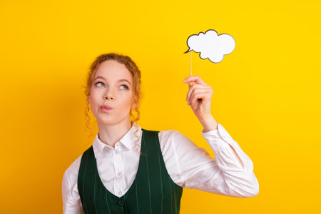 Young red-haired female student holding a speech bubble cutout, posing playfully against a vibrant...