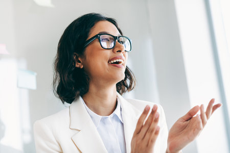 Charming businesswoman in modern office setting, applauding and expressing positivity, dressed in a professional white suitの写真素材