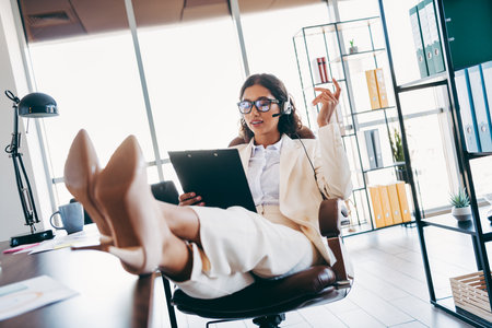 Confident Businesswoman in Stylish Suit Using Hands free Headset During Office Work with Relaxed and Professional Demeanorの写真素材