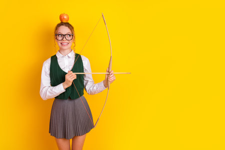 Teenager in school uniform with bow and apple on yellow background showcasing creativity and playful educationの写真素材