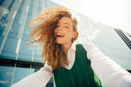 Cheerful businesswoman enjoying a sunny day outdoors, wearing a green waistcoat, embracing urban style with eleganceの写真素材
