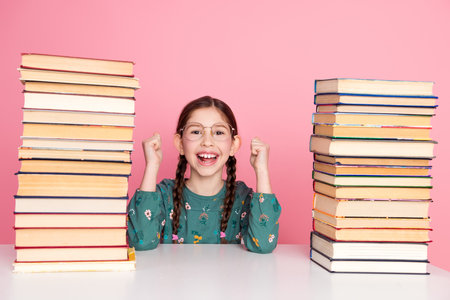 Excited preteen girl with braided hair next to stacks of book against a pink background showcasing education conceptの写真素材