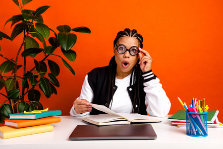 Young female student surprised while studying at desk with colorful book and laptop in a vibrant...