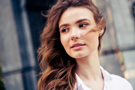 Charming young woman enjoying a sunny urban day with relaxed elegance in casual attire amidst an...