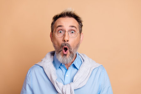 Surprised mature gentleman in casual attire expressing astonishment against beige background for lifestyle and business conceptsの写真素材