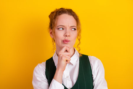 Portrait of a young student with red hair posing in thoughtful gesture on a vibrant yellow...