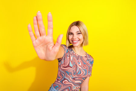 Smiling young woman gestures with her hand on a bright yellow background, wearing a stylish...