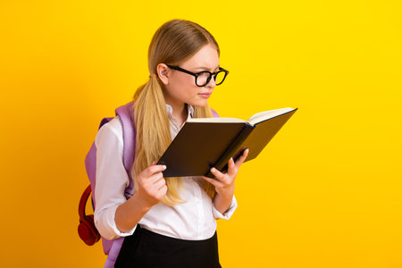 Young student deeply engaged in reading a book on a vibrant yellow background, fostering knowledge and academic growthの写真素材