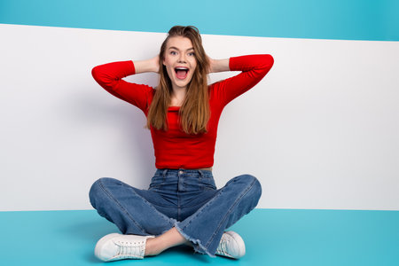 Joyful cheerful woman in casual attire enjoying a carefree moment seated on a colorful modern backgroundの写真素材