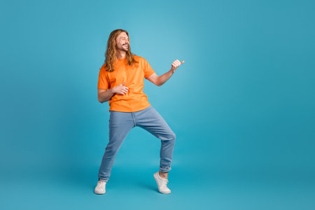 Young man in orange t-shirt posing playfully against a blue background with a cheerful expression and fun vibeの写真素材