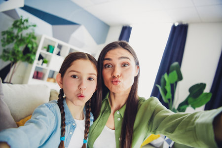 Mother and daughter making funny faces in a cozy home setting, showcasing bonding, love, and family...