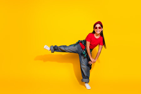 Cheerful young girl in casual style clothing posing in a fun stance against a vibrant yellow background, joyful and playfulの写真素材