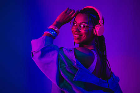 Young woman wearing headphones enjoying music in neon light with vibrant colors and stylish casual...