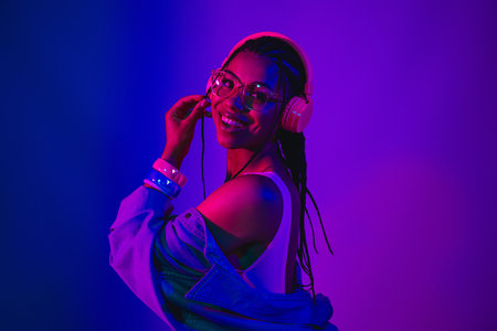 Vibrant young woman enjoying music with headphones under neon purple and blue lights showcasing...