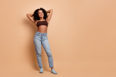 Stylish young woman in casual outfit on beige background showcasing beauty, fashion, and a cheerful and confident demeanorの写真素材