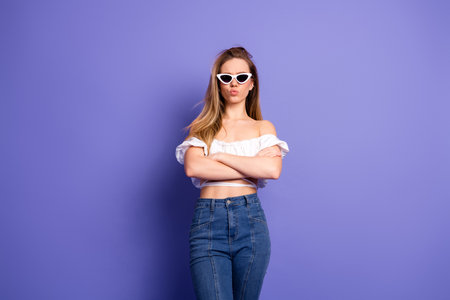 Chic Young Woman in Casual Off-the-Shoulder Top with Sunglass Posing Against Purple Background in a...