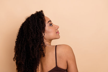 Portrait of a young woman with curly hair wearing a brown top against a beige background, exuding confidence and eleganceの写真素材