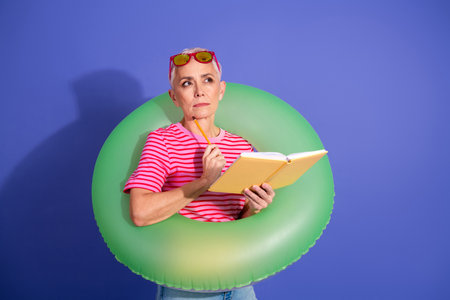A stylish senior woman with short gray hair reading a book while wearing a green inflatable ring...