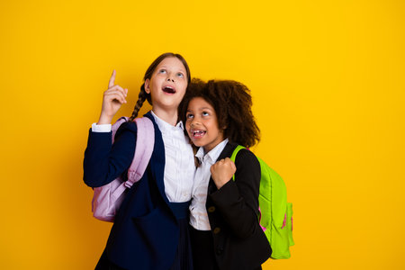 Two cheerful schoolgirls smiling and looking up, showcasing friendship and joy against a vibrant yellow backgroundの写真素材