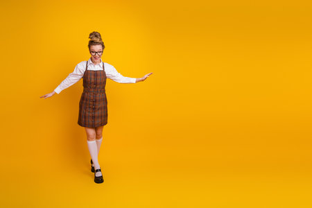 Charming young student in plaid formal outfit stands gracefully on a vibrant yellow background, radiating positivityの写真素材