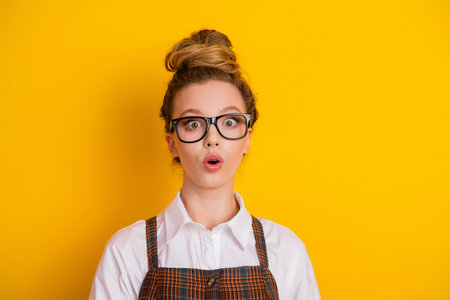 Surprised student wearing glasses stands against a yellow background, showcasing a cheerful and youthful expression.の写真素材