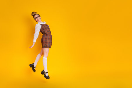 Cheerful young woman posing in plaid dress against a yellow background showing trend and youthful energy.の写真素材