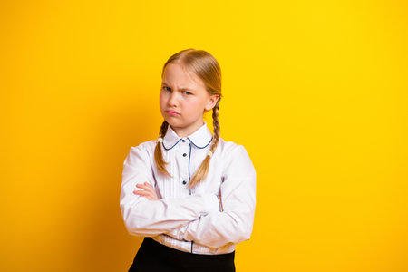 Adorable schoolgirl with braids expressing dissatisfaction against a vibrant yellow background, wearing a stylish white uniformの写真素材