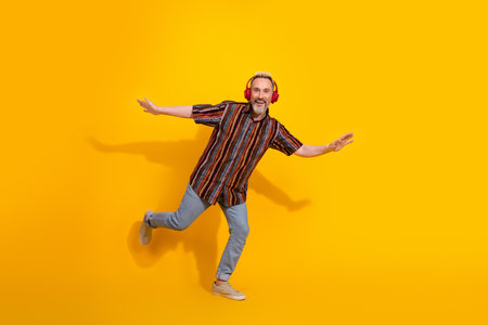 Charismatic middle aged man with headphones gesturing playfully against a vibrant yellow backgroundの写真素材