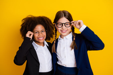 Two cheerful female classmates in school uniforms posing with glasses against a vibrant yellow backgroundの写真素材
