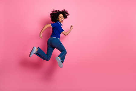 Joyful young woman jumps energetically against pink background showcasing casual style and bright...