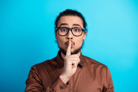 Man in formal outfit making quiet gesture against teal background expressing secrecy concept